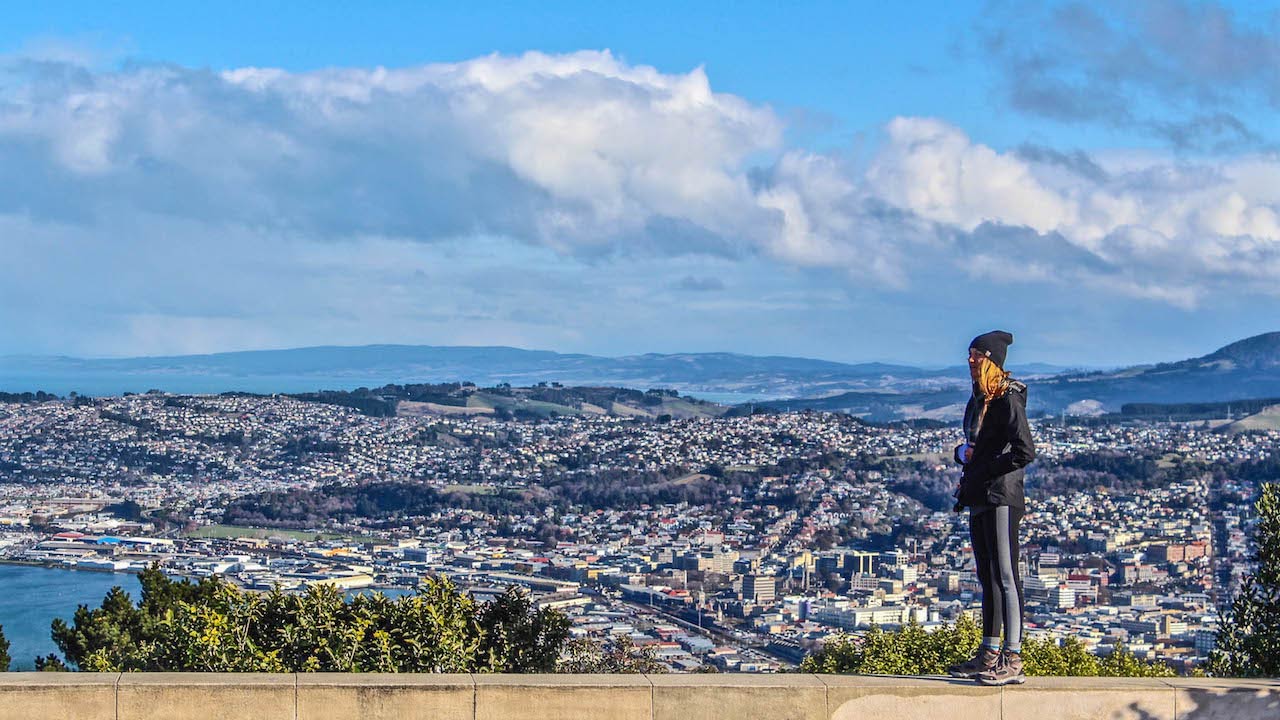 A woman stands on a platform looking out over the city of Dunedin, New Zealand
