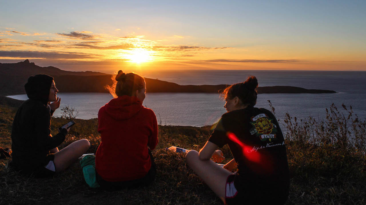 Two women sit looking out at a beautiful sunset over a lake near Otago, New Zealand