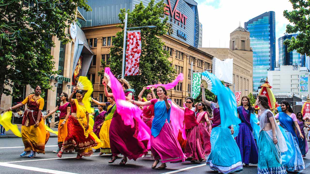 Colorfully dressed women dance in the street during a parade in Auckland, New Zealand
