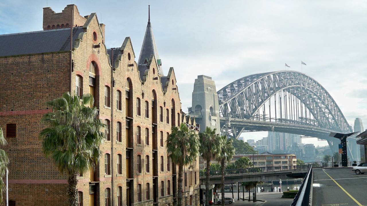The sun hitting a row of brick buildings and the Sydney Harbor Bridge in the background