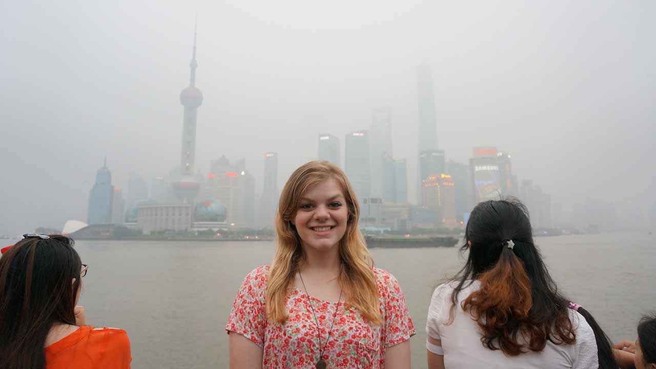 A woman smiles in front of a hazy Shanghai cityscape