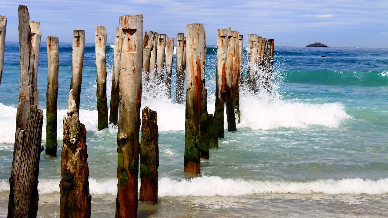 Waves crash into the remaining posts of a wooden boardwalk in Dunedin, New Zealand