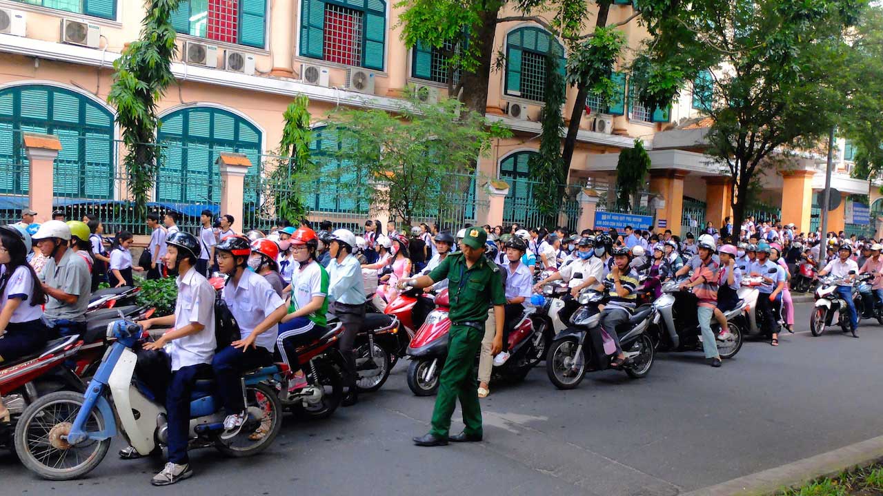 A police officer directs traffic as a hoard of motorbikes drive by on a street in Ho Chi Minh City