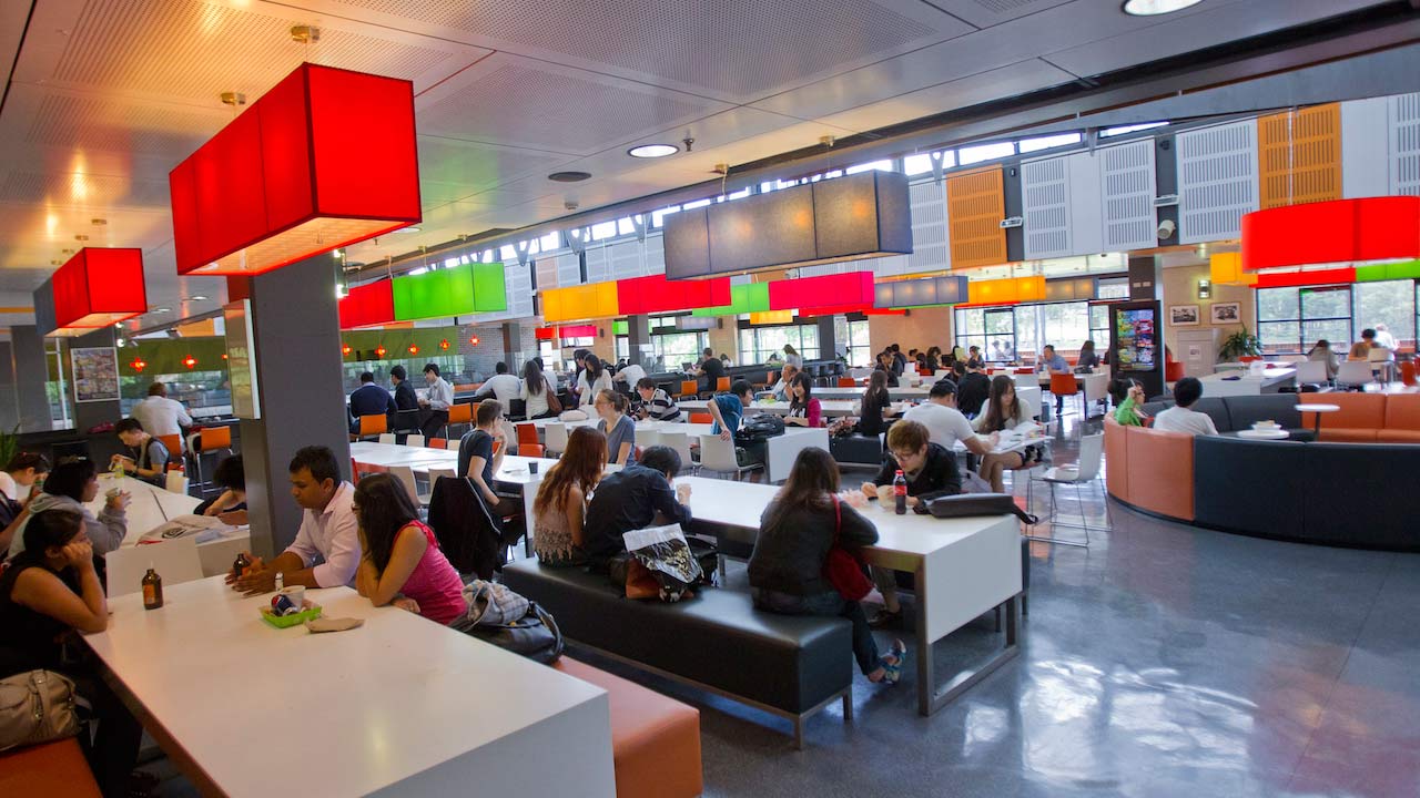 A crowded dining hall is filled with students conversing and eating at Macquarie University near Sydney, Australia