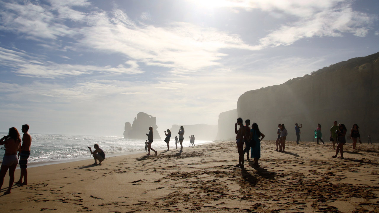 Many people stand along the beach enjoying the beautiful view of the 12 Apostles on a sunny day