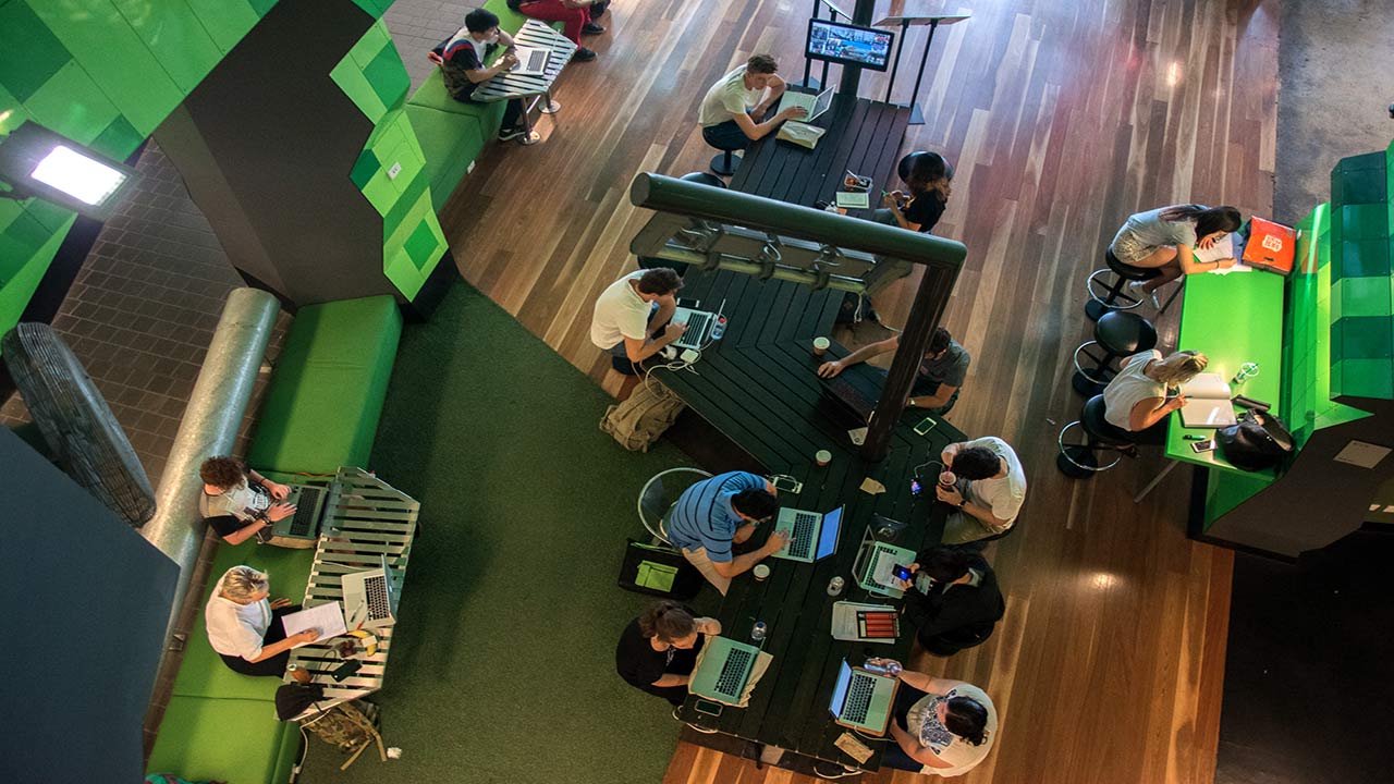 An aerial view of students on their computers or gathered studying at tables in a common area of RMIT's campus