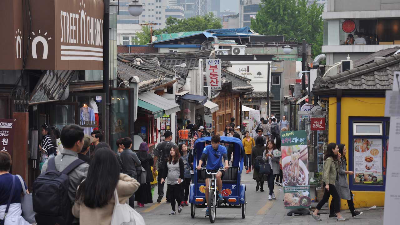A man rides a bicycle attached to a transport for passengers up a busy street in Seoul