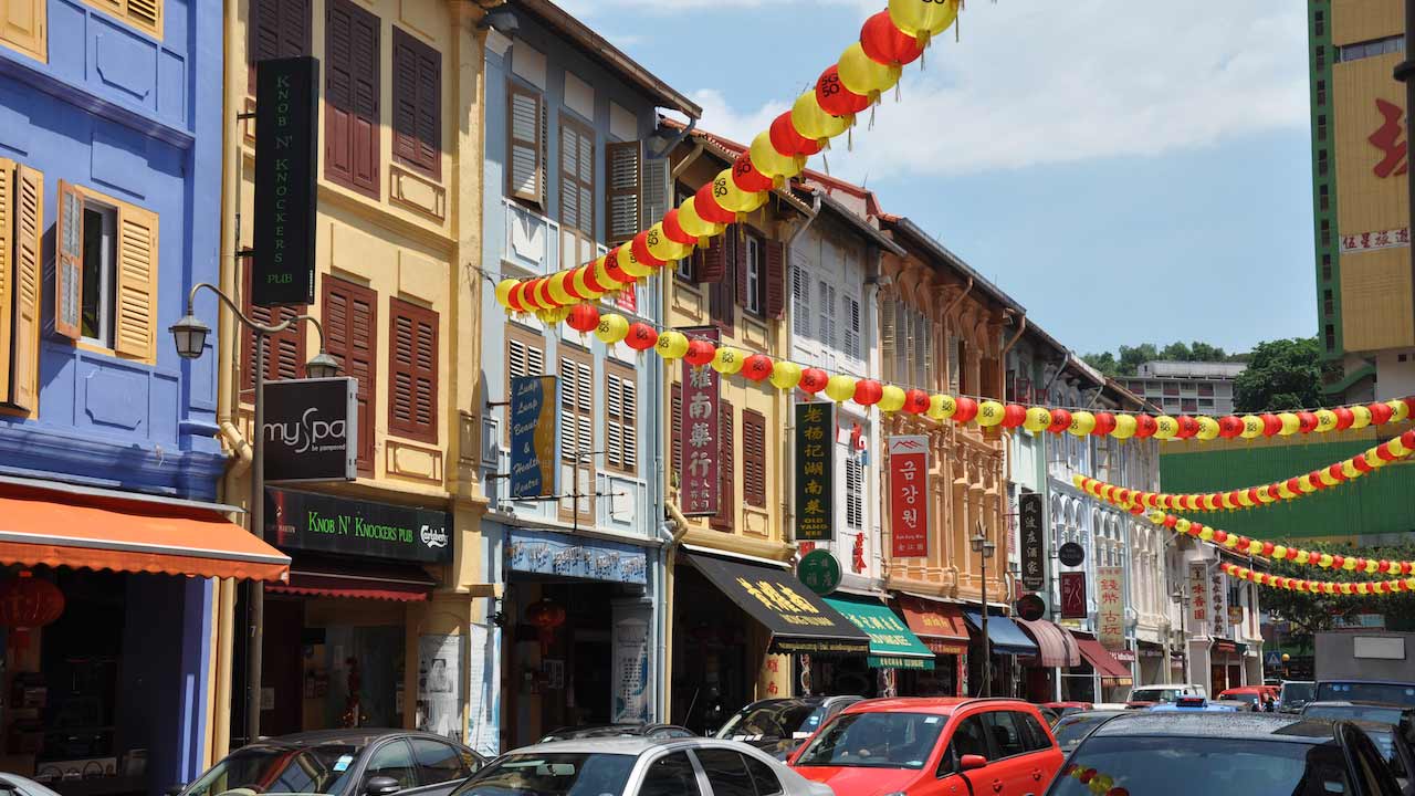 Yellow and red flags hang between buildings on a tiny street in Singapore