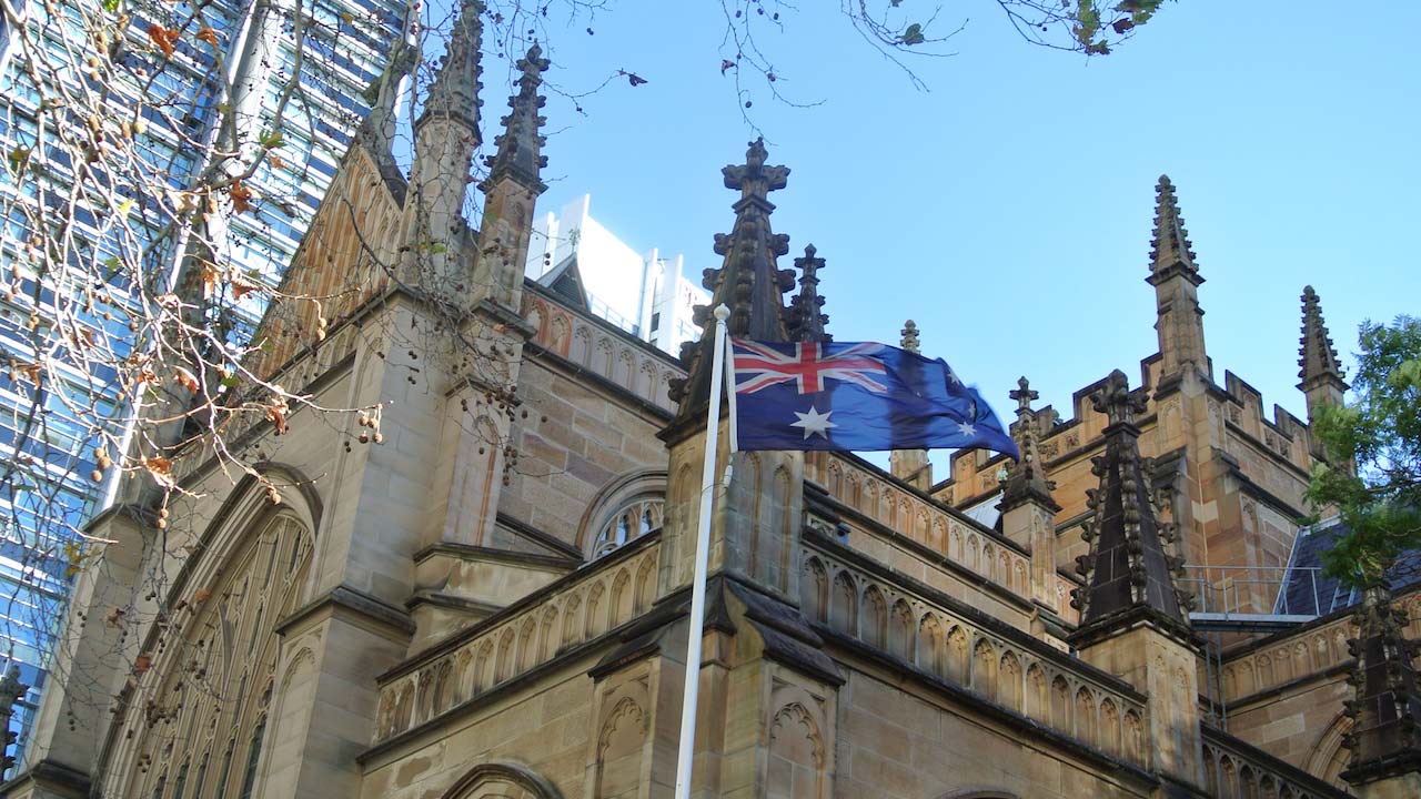 The Australian flag waves in the wind in front of an ornate church in Sydney