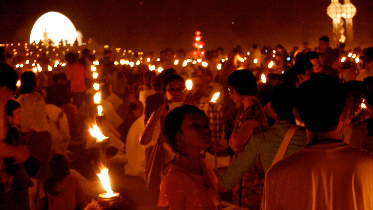 Crowds of people hold candles for a nighttime ceremony in Thailand