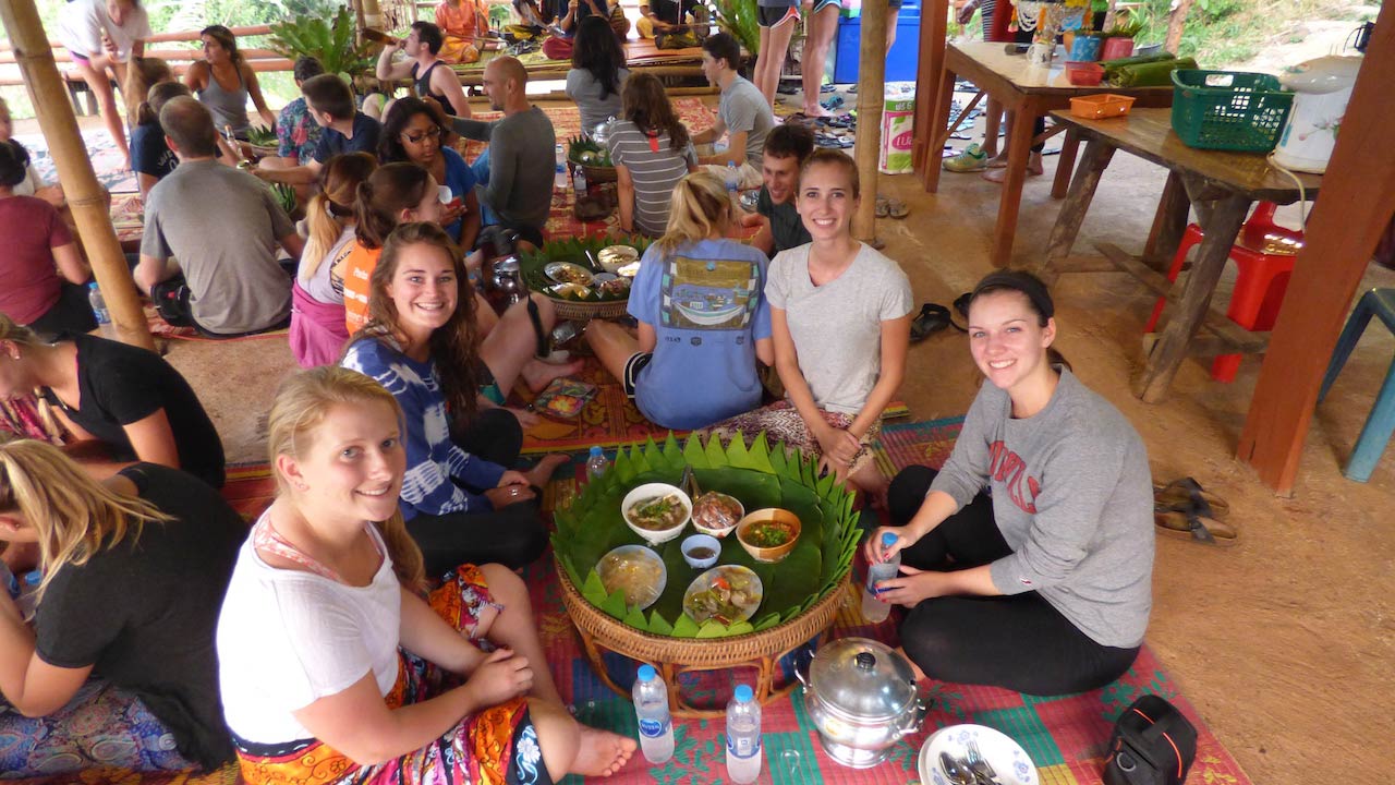 A group of women sit on the ground around a traditional khantoke dinner in northern Thailand