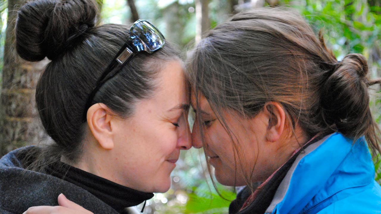 A closeup of two women touching their foreheads together, eyes closed and smiling