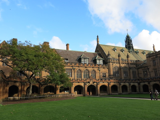 A group of students walk toward a large, ornate building on University of Sydney's campus