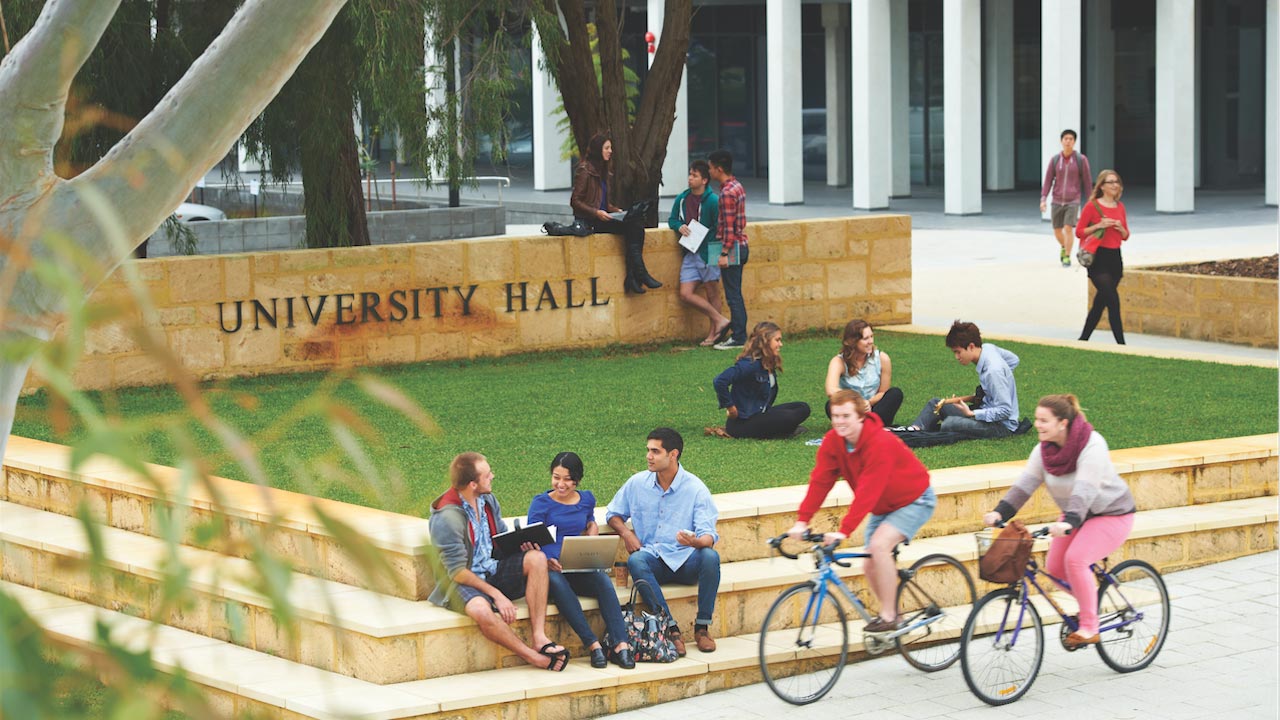 People gather on the grassy quad, two cyclists ride by on University of Western Australia's campus in Perth