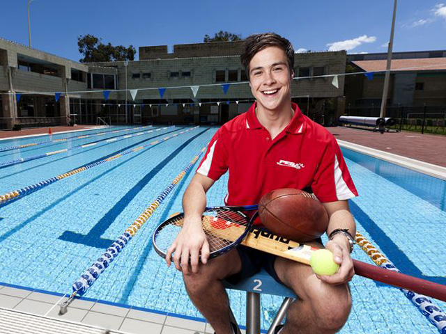 A man sits in front of an outside lap pool holding an array of athletic equipment