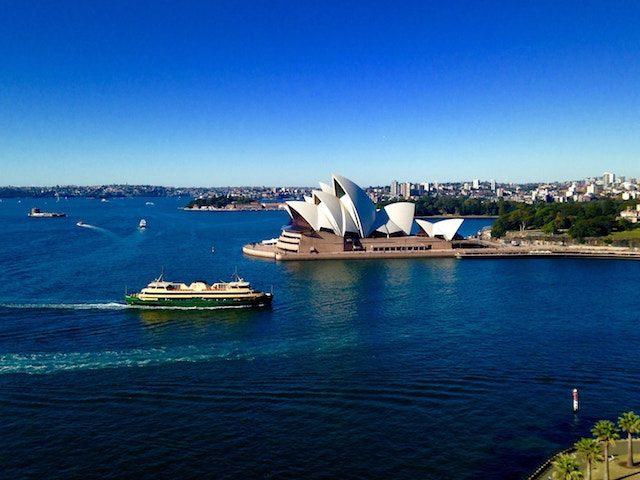 A boat cruises by the Sydney Opera House on a beautiful blue sky day