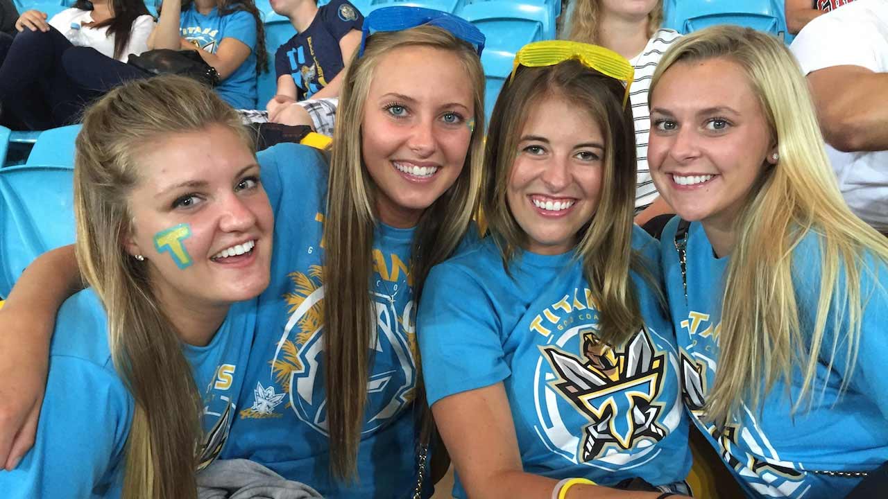 Four women smile together in spirited gear during the Gold Coast Titans Rugby Match
